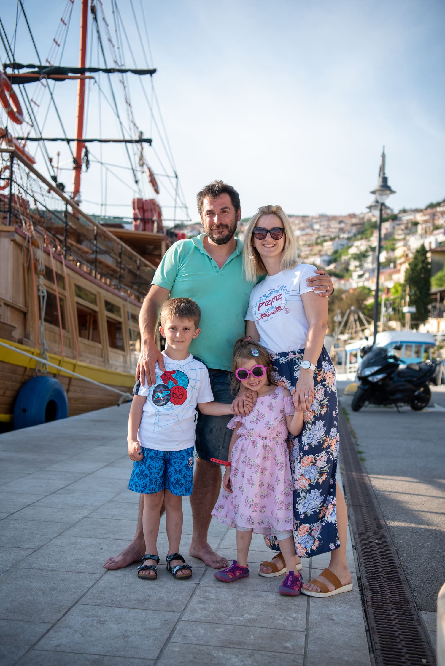 Dražen Čikor mit Frau und zwei Kindern am Kai von Rabac — das hölzerne Segelboot hinter ihnen, das Dorf am Hang darüber.