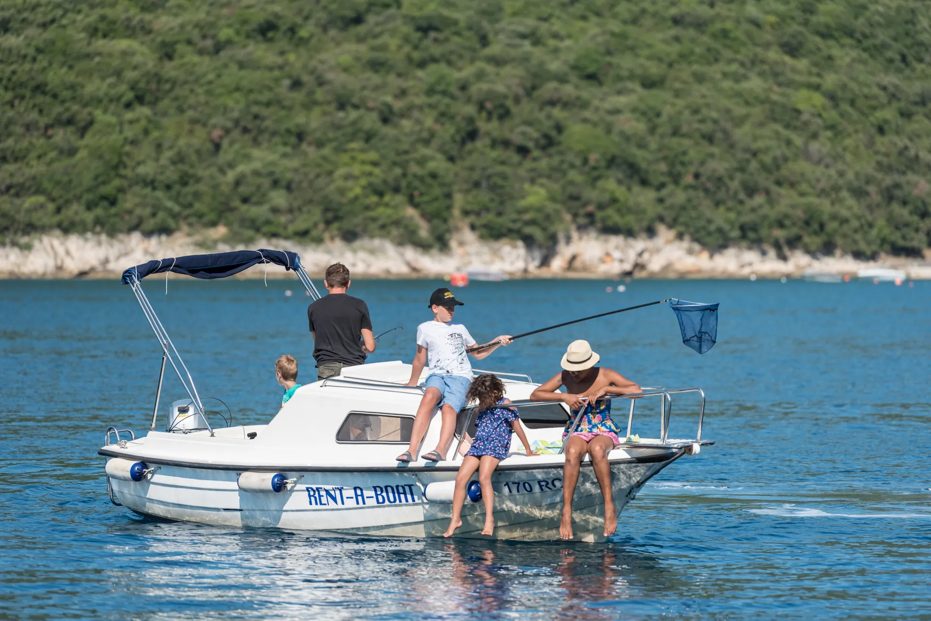 Dalmatinka anchored off a quiet shore — kids fishing with a hand-net.