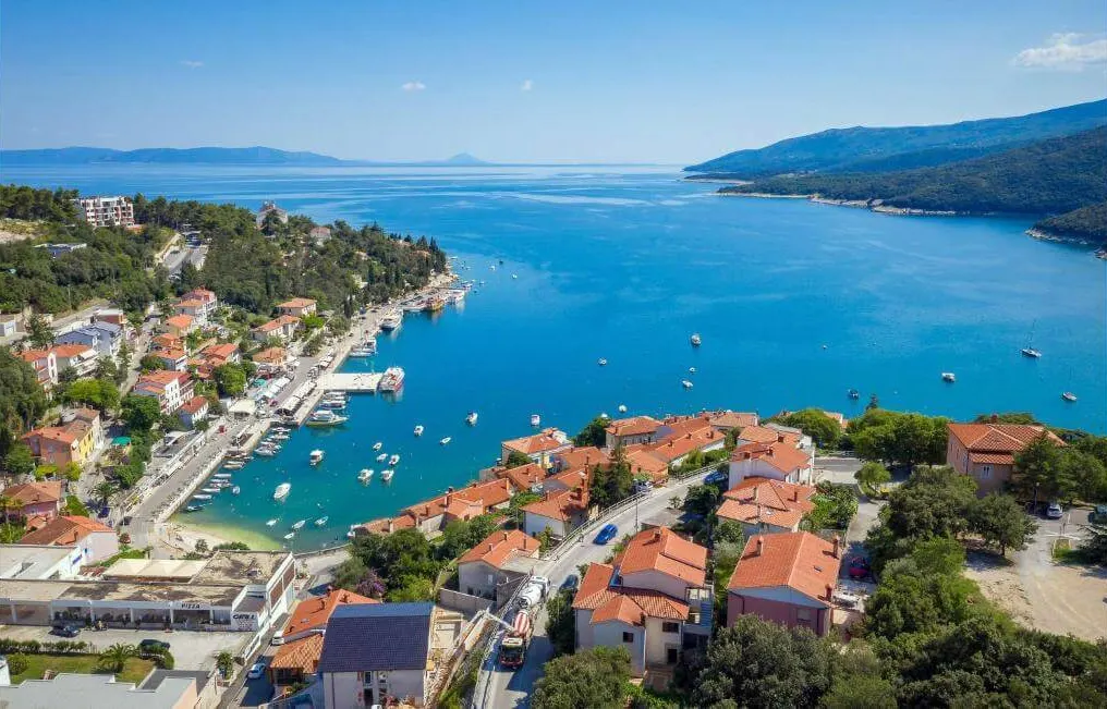 Rabac harbour and its boat-filled bay from above — Eastern Istrian coast curving toward Učka in the distance.